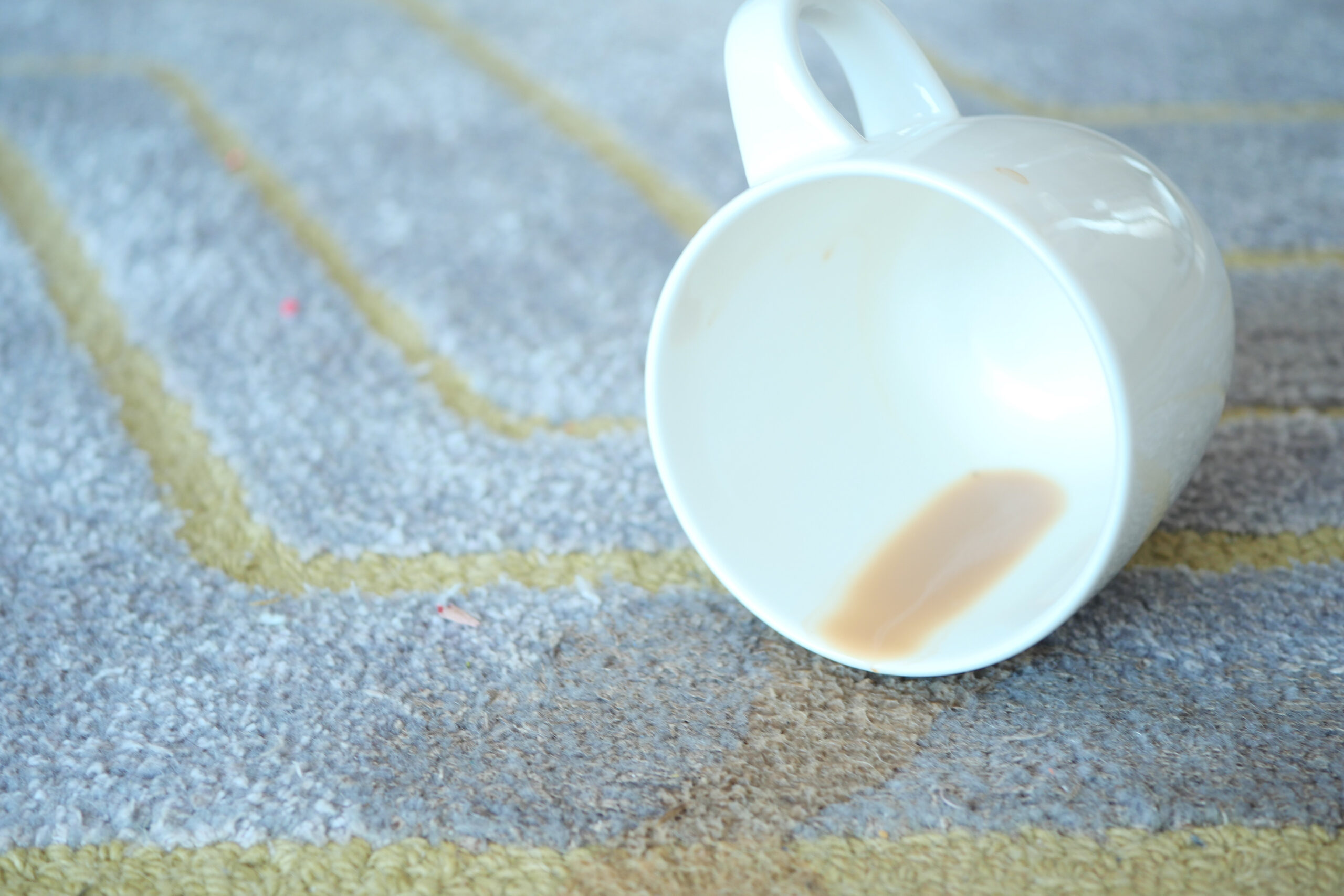cup of coffee spilled on gray color carpet .